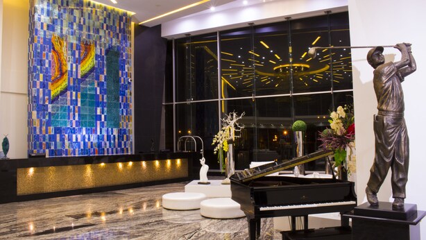 Un vaste hall d’entrée agrémenté d’un grand piano, d’une statue et d’un mur décoré d’une mosaïque aux couleurs vives.