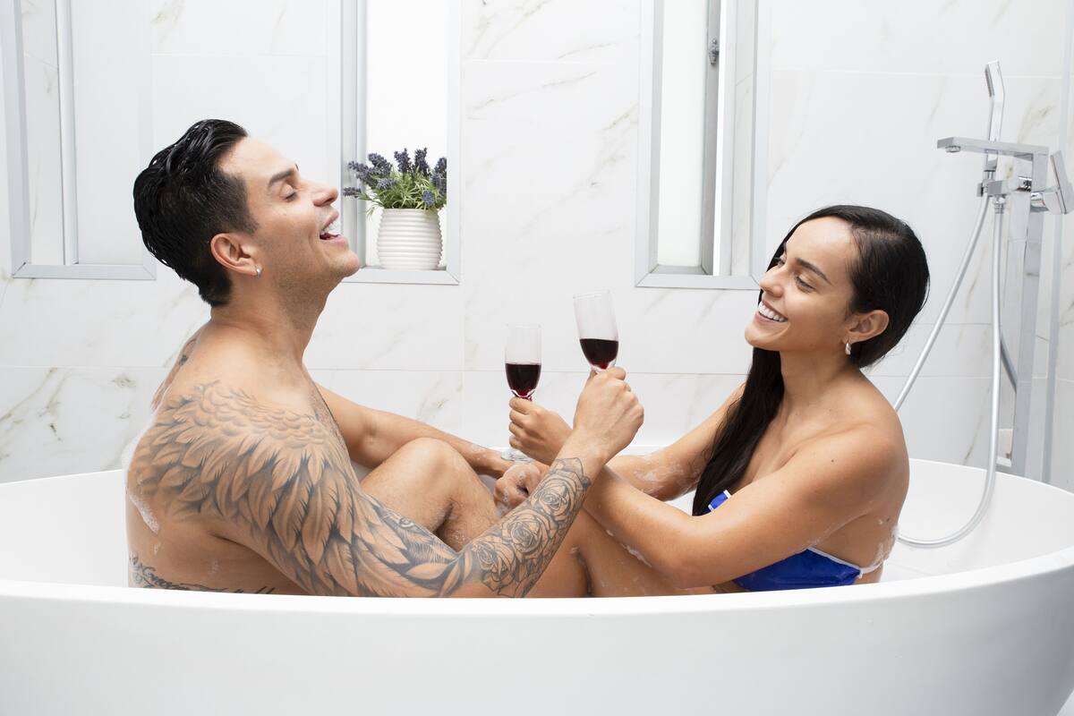 Una pareja en una bañera con ventana y una planta al fondo.