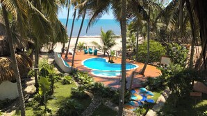Zona de piscina con diseño circular, rodeada de palmeras y vistas a la playa.