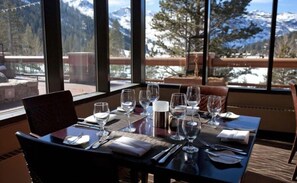 A dining table set for four with wine glasses, water glasses, and cutlery, overlooking a snowy mountain landscape. - Resort at Squaw Creek Penthouse 810 (Olympic Valley)