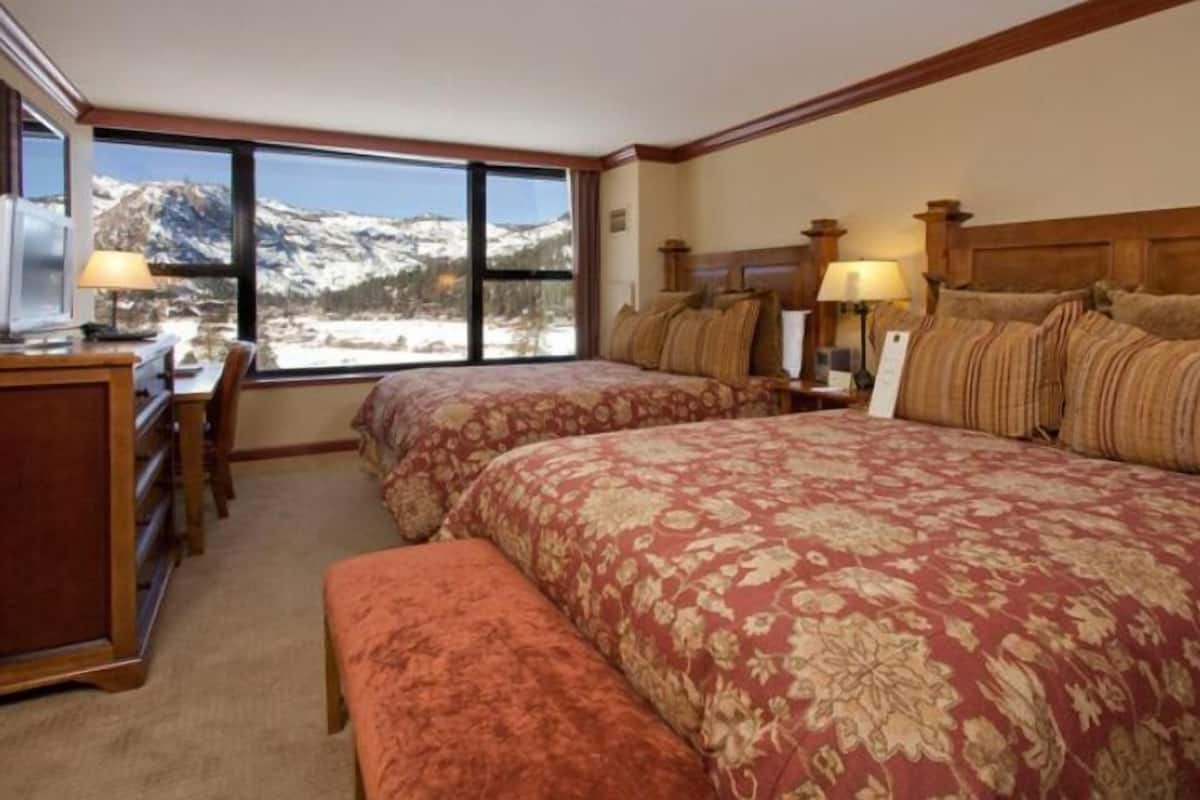 Une chambre d’hôtel avec deux lits, un bureau et une vue sur des montagnes enneigées.