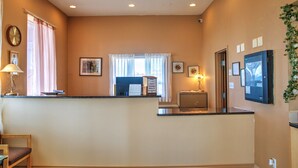 Zona de recepción de un hotel con mostrador, escritorio, silla, reloj y cuadros en la pared.