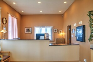 A hotel reception area with a counter, a desk, a chair, a clock, and framed pictures on the wall.