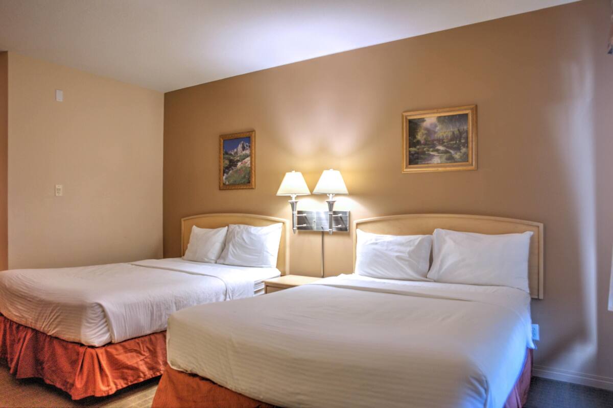 Habitación de hotel con dos camas, una mesita de noche con lámparas y dos cuadros en la pared.
