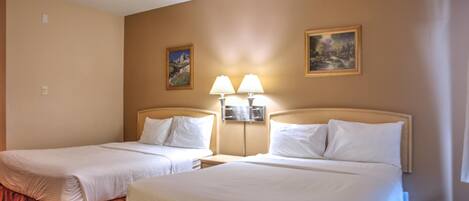 Ein Hotelzimmer mit zwei Betten, einem Nachttisch mit Lampen und zwei gerahmten Bildern an der Wand.
