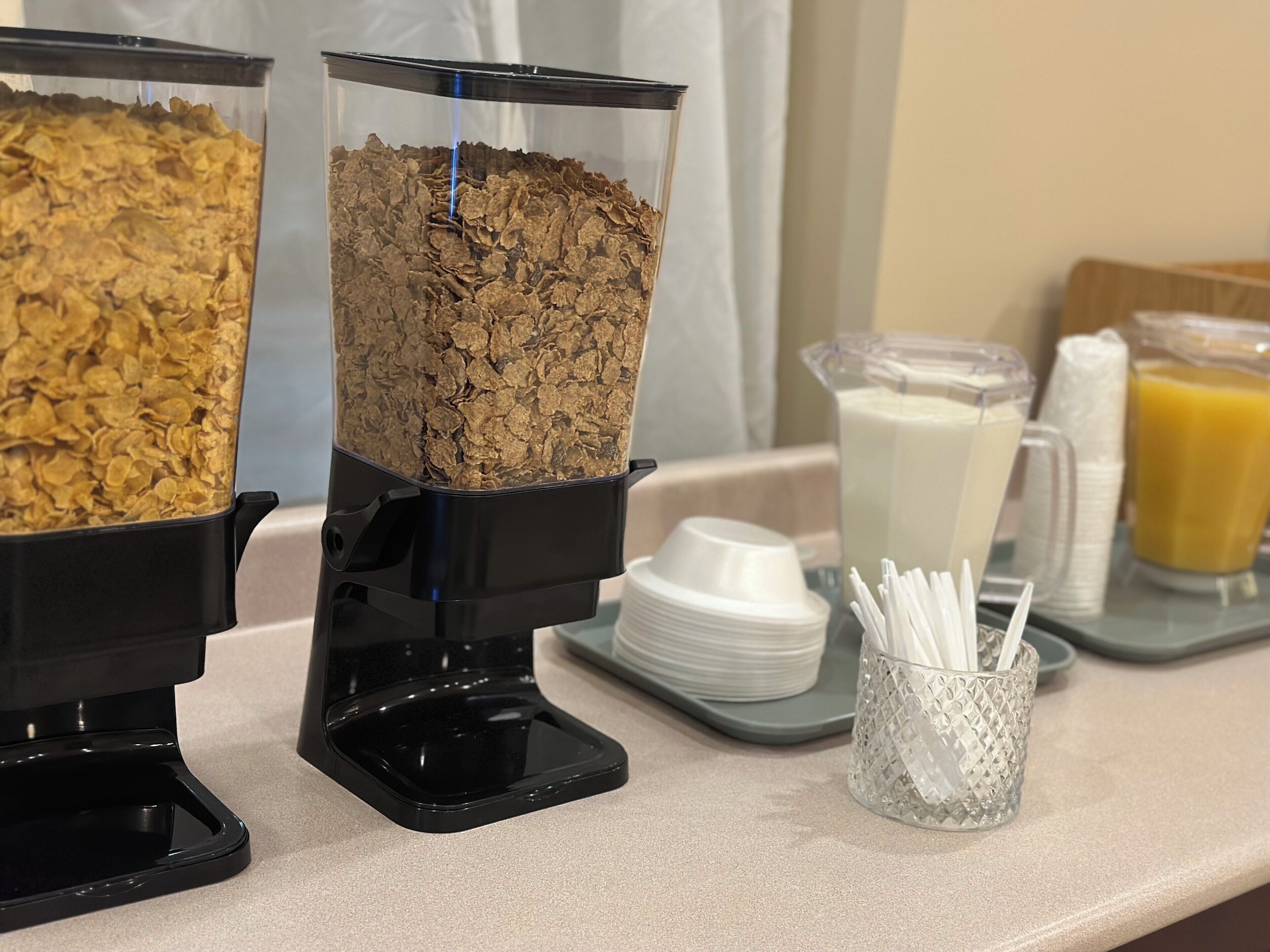 Montaje de un bufé de desayuno con dispensadores de cereales y recipientes para leche y jugo.