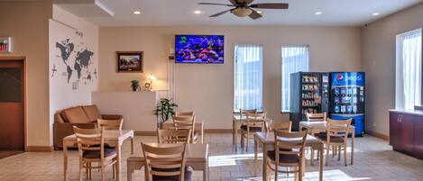 Un hall de hotel con zona de comedor, televisión, mapa en la pared y máquinas expendedoras.