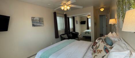 A hotel room with a large bed, a ceiling fan, a TV, and a painting on the wall.