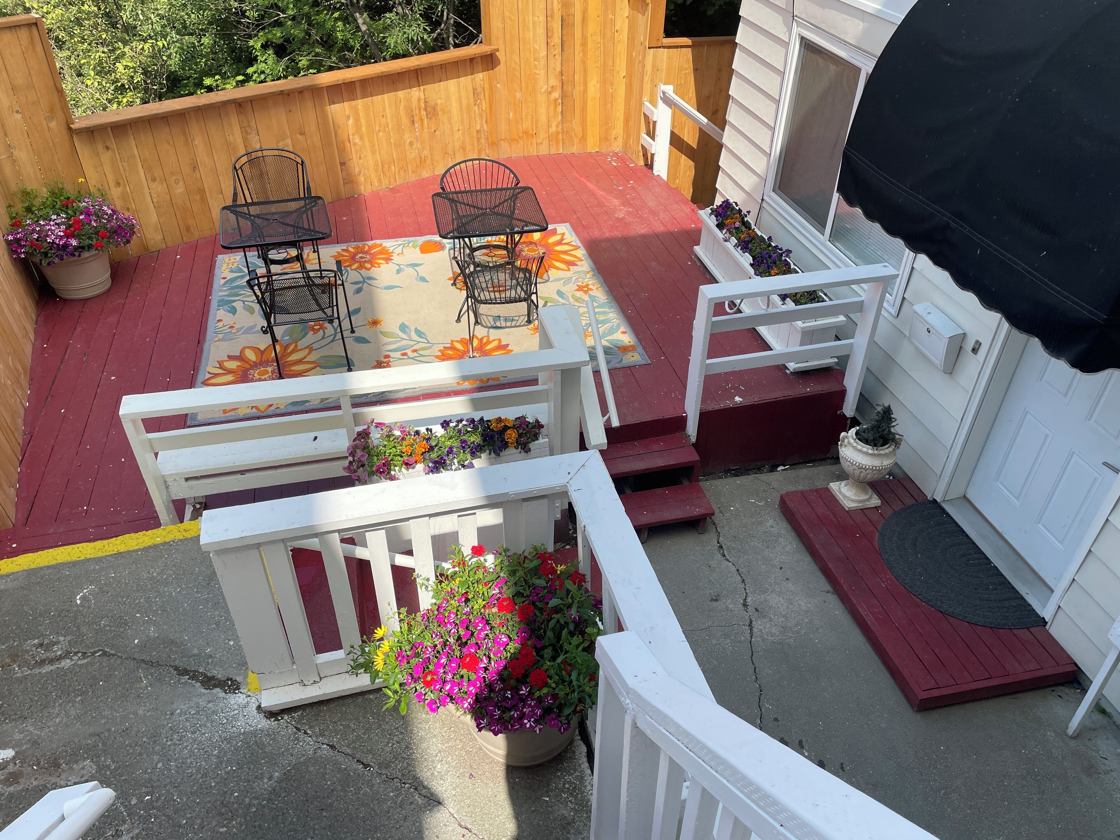 Un patio con mobiliario exterior, una terraza de madera y macetas con flores.