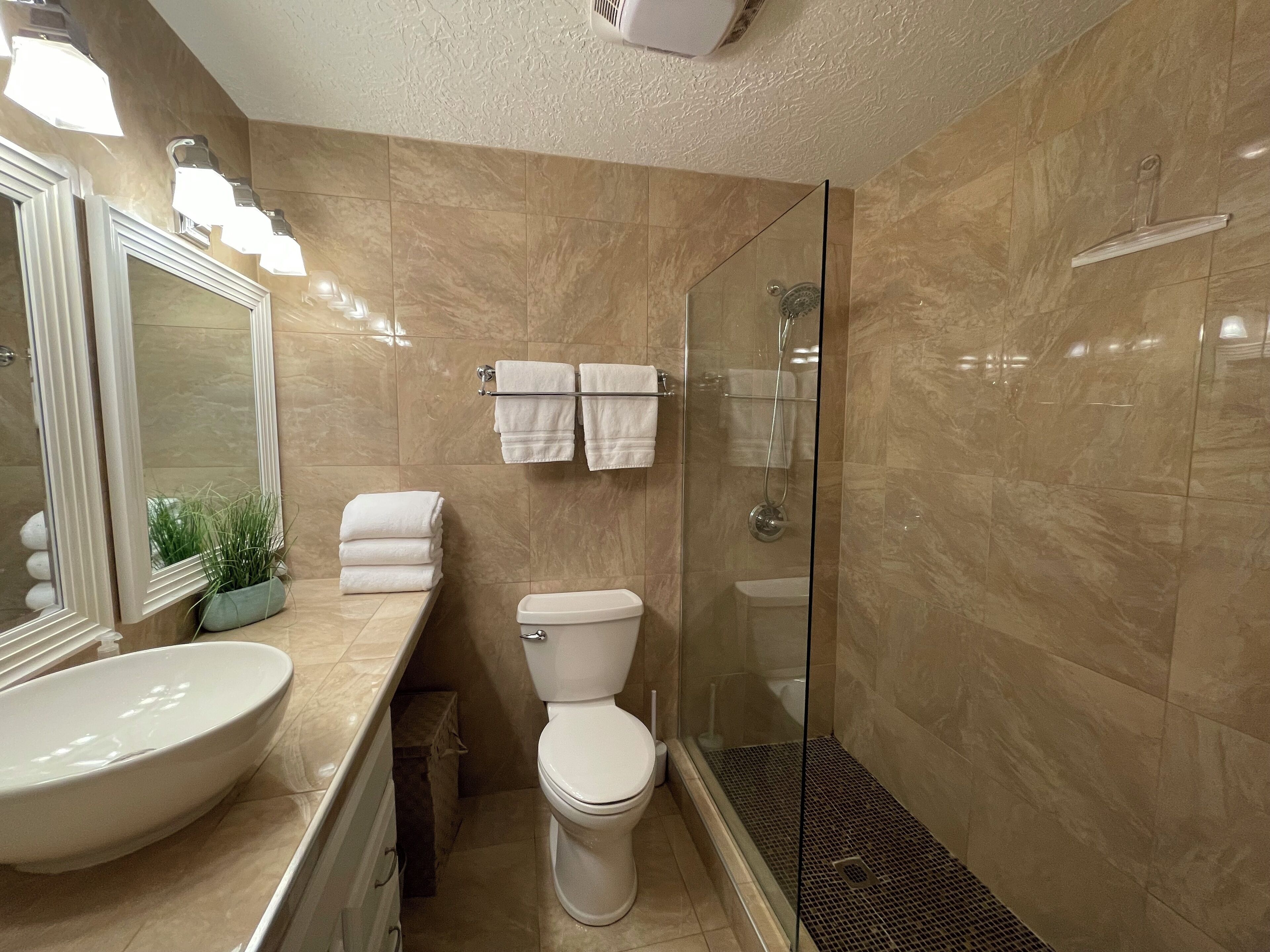 A modern bathroom with a large mirror, a sink, a toilet, and a glass-enclosed shower.