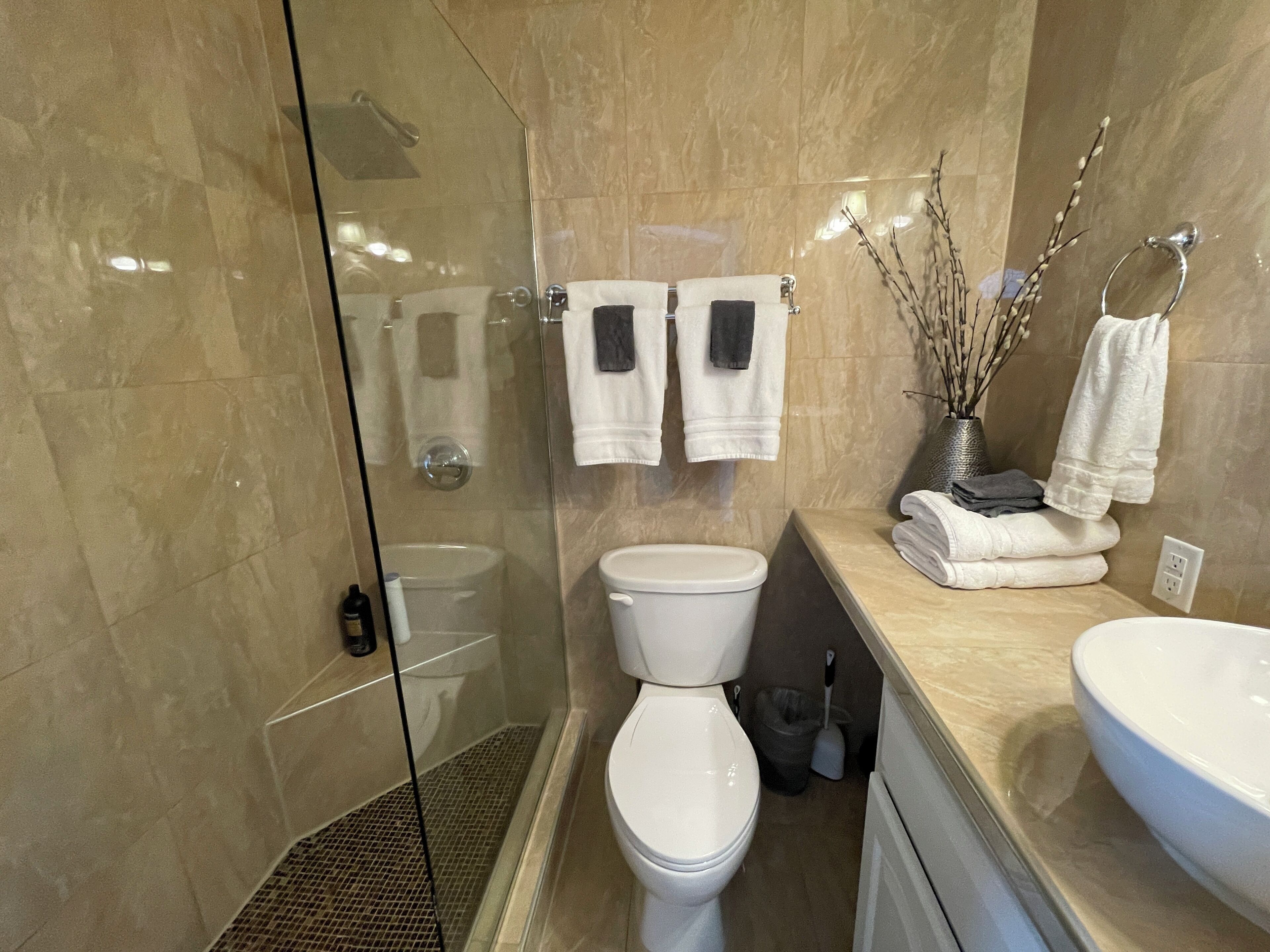 Um banheiro moderno com chuveiro em box de vidro, vaso sanitário e pia.