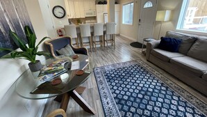 A living room with a glass coffee table, a sofa, a patterned rug, and a dining area with chairs and a kitchen in the background. - Arctic Fox Inn (Anchorage)