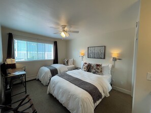 A hotel room with two beds, a desk, a chair, a ceiling fan, a window with blinds, and wall-mounted lamps. - Arctic Fox Inn (Anchorage)