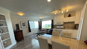 A modern kitchen with white cabinets, a dining area with a glass table, and a living room with a sofa and a view of the outdoors. - Arctic Fox Inn (Anchorage)