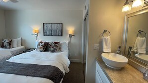 A hotel room with a bed, a bedside table, a lamp, a painting on the wall, a bathroom with a sink and mirror. - Arctic Fox Inn (Anchorage)