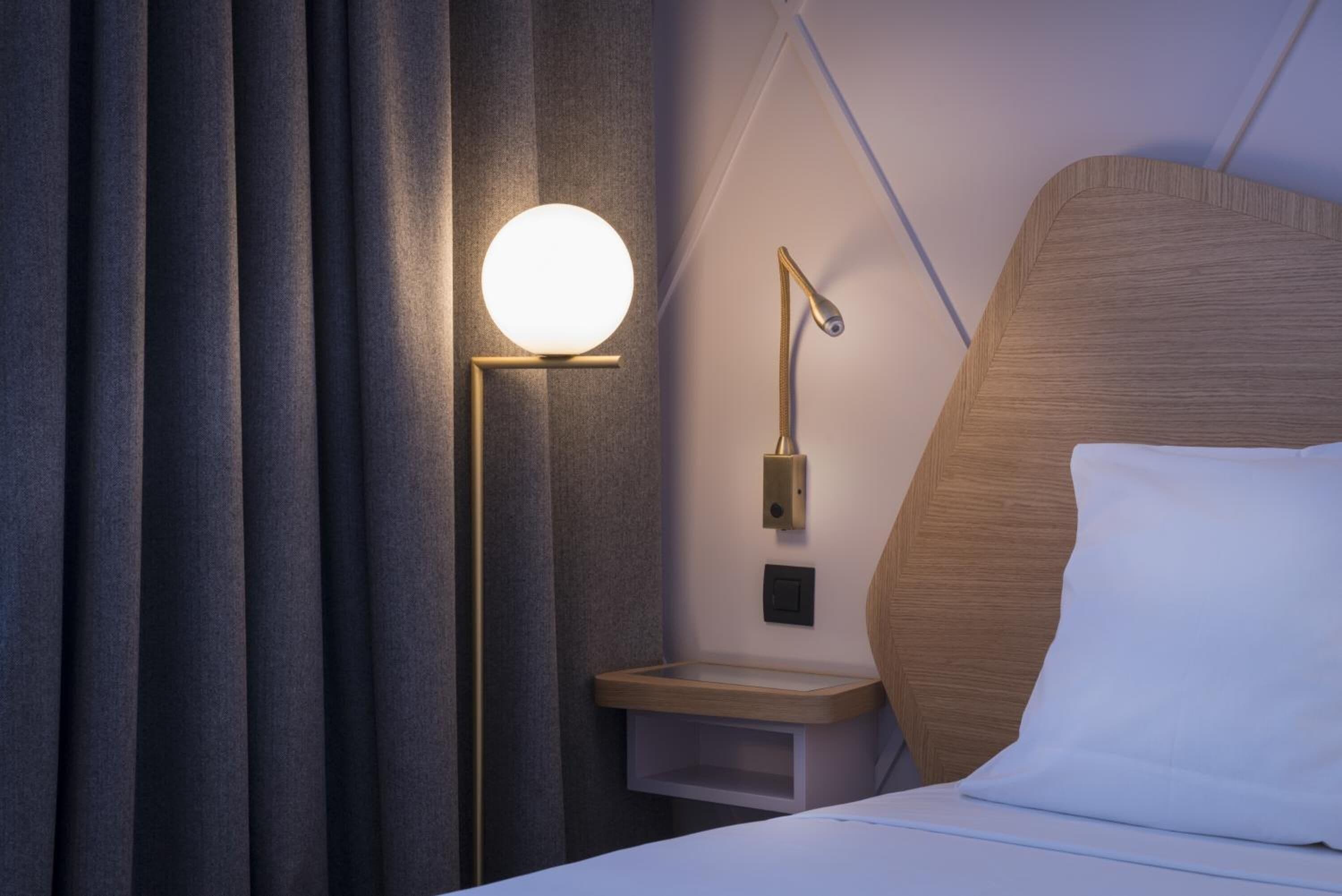 Une chambre d’hôtel moderne avec un grand lit, une table de chevet avec une lampe et une petite table fixée au mur.