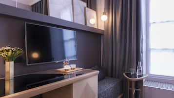 Een moderne hotelkamer met een flatscreen televisie, een klein barretje met een dienblad, een bank en een raam met gordijnen.