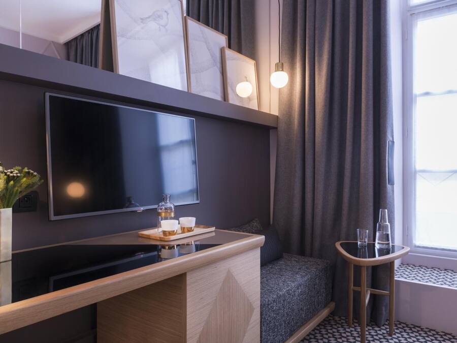 Ein modernes Hotelzimmer mit Flachbildfernseher, einer kleinen Bar mit Tablett, einer Sitzecke und einem Fenster mit Vorhängen.