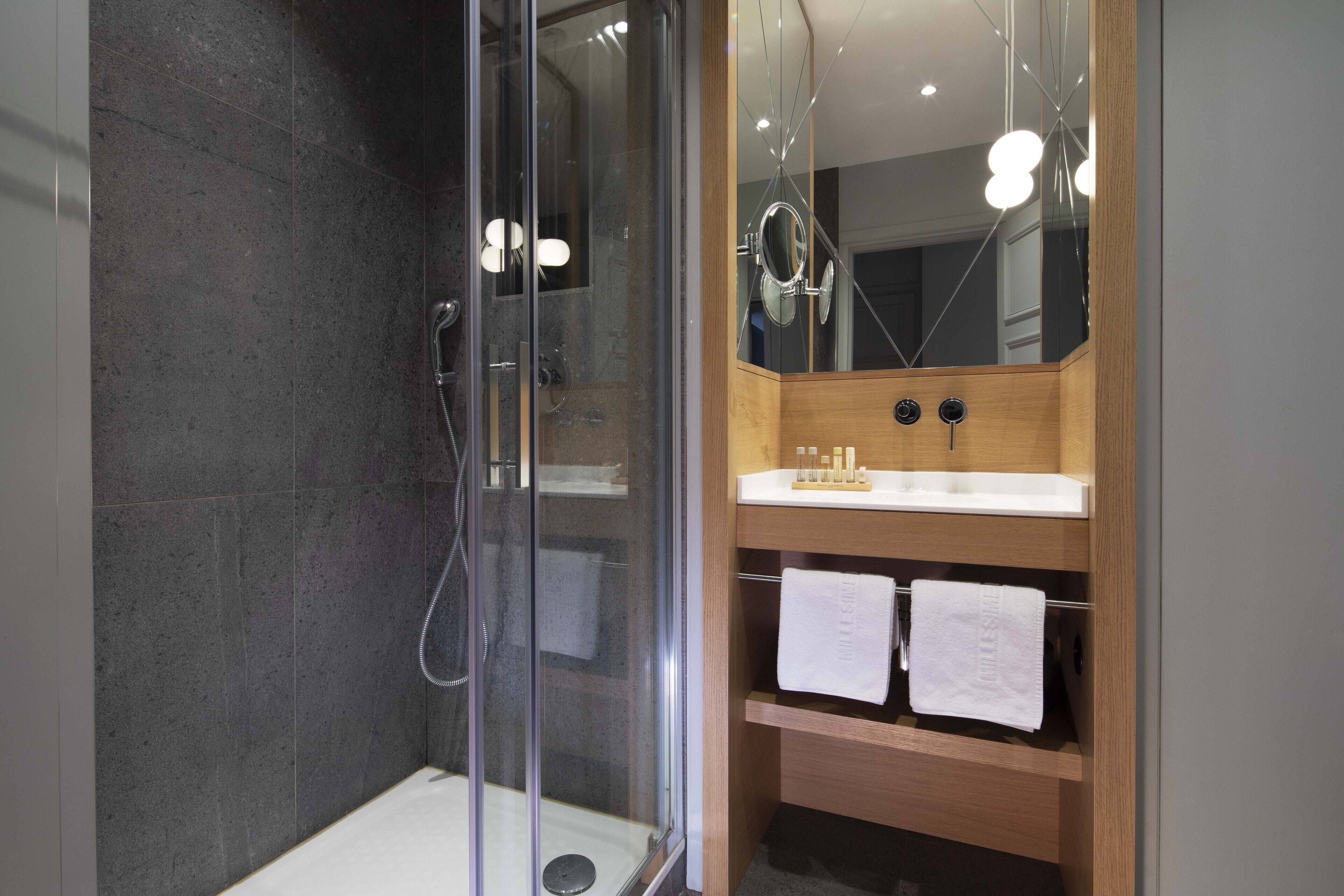 A modern bathroom with a glass-enclosed shower, a wooden vanity with a white sink, and two towels hanging on the shelf.