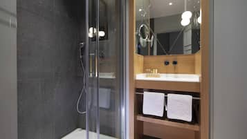 A modern bathroom with a glass-enclosed shower, a wooden vanity with a white sink, and two towels hanging on the shelf.