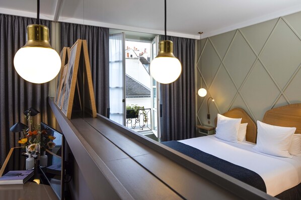 A hotel room with a bed, bedside tables, a mirror, curtains, and a view of a balcony with plants.