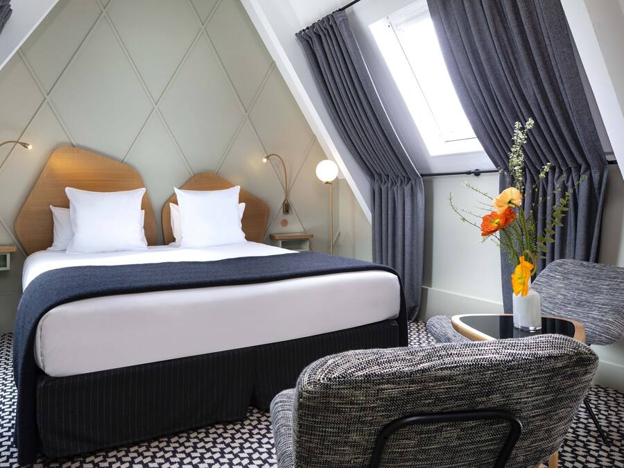 Un hotel moderno con una cama grande, dos mesitas de noche con lámparas, una pequeña mesa redonda con un florero y un piso con diseño.