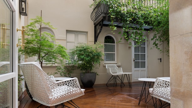 An outdoor patio with wooden flooring, white wicker chairs, and a potted plant. - Millésime Hôtel (Paris)