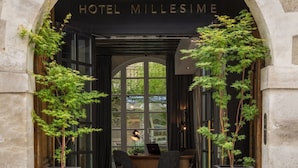 The entrance to Hotel Mille Signe, featuring an arched doorway, two potted plants, a reception desk with chairs, and a view through the windows. - Millésime Hôtel (Paris)
