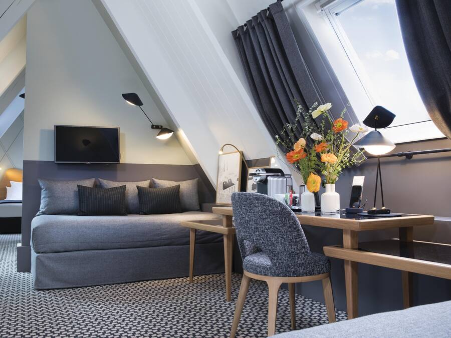 A modern bedroom with a bed, desk, chair, and a TV.