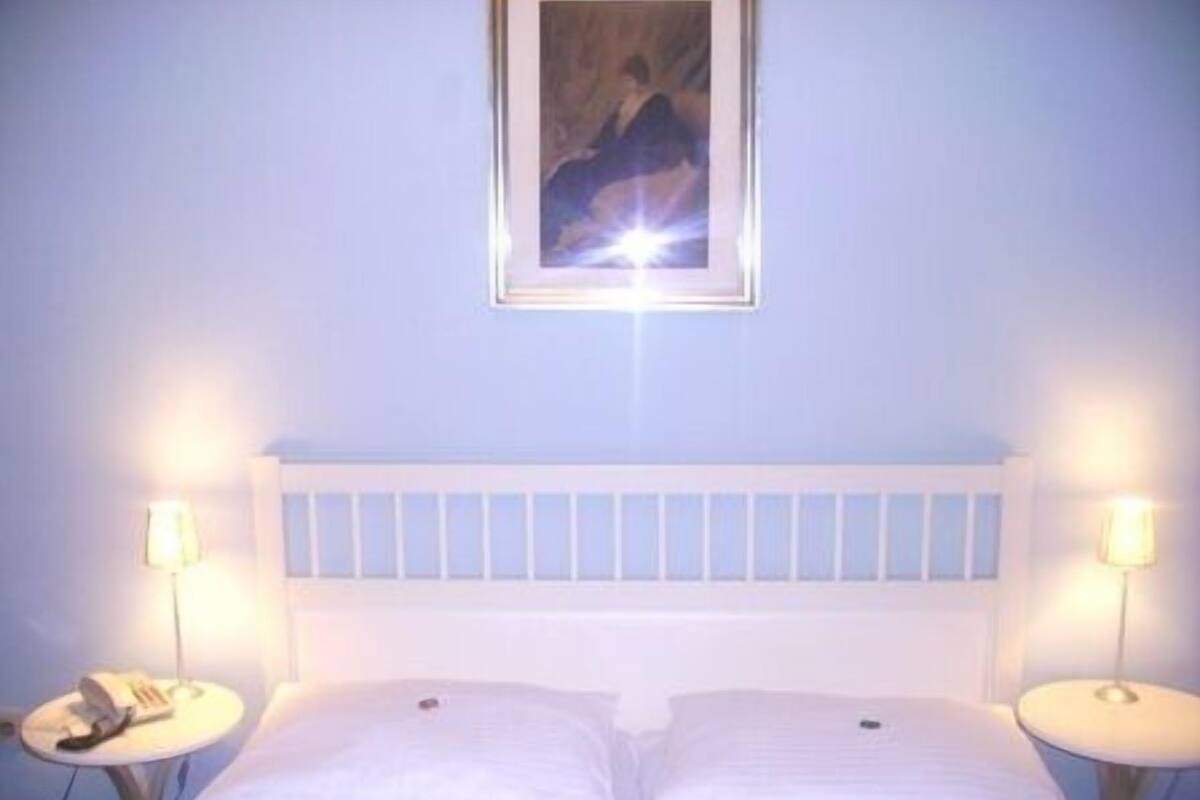 Una cama con ropa de cama blanca, dos mesitas de noche y un marco de cuadro en la pared.