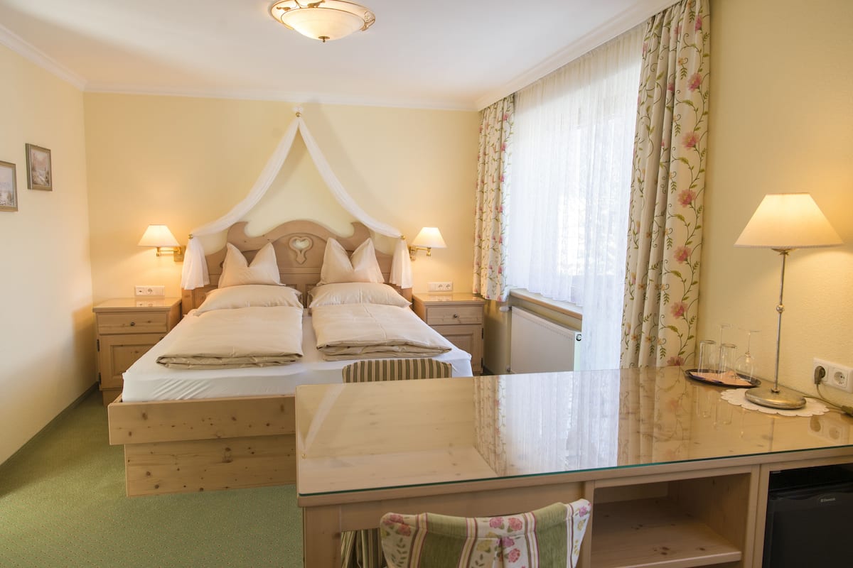 A bedroom with a canopy bed, bedside lamps, a glass table, and a view of the room.