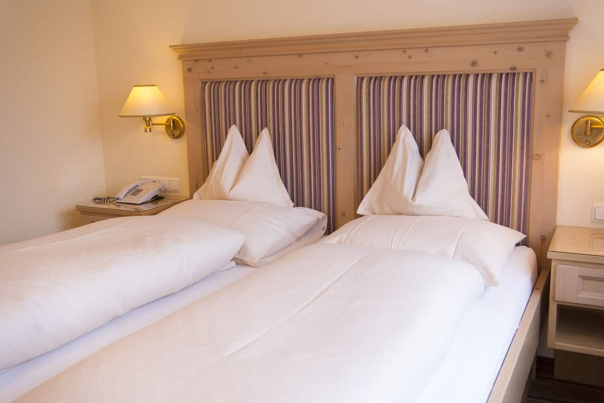 A hotel room with two single beds, a bedside table with a lamp, a phone, and a small shelf.