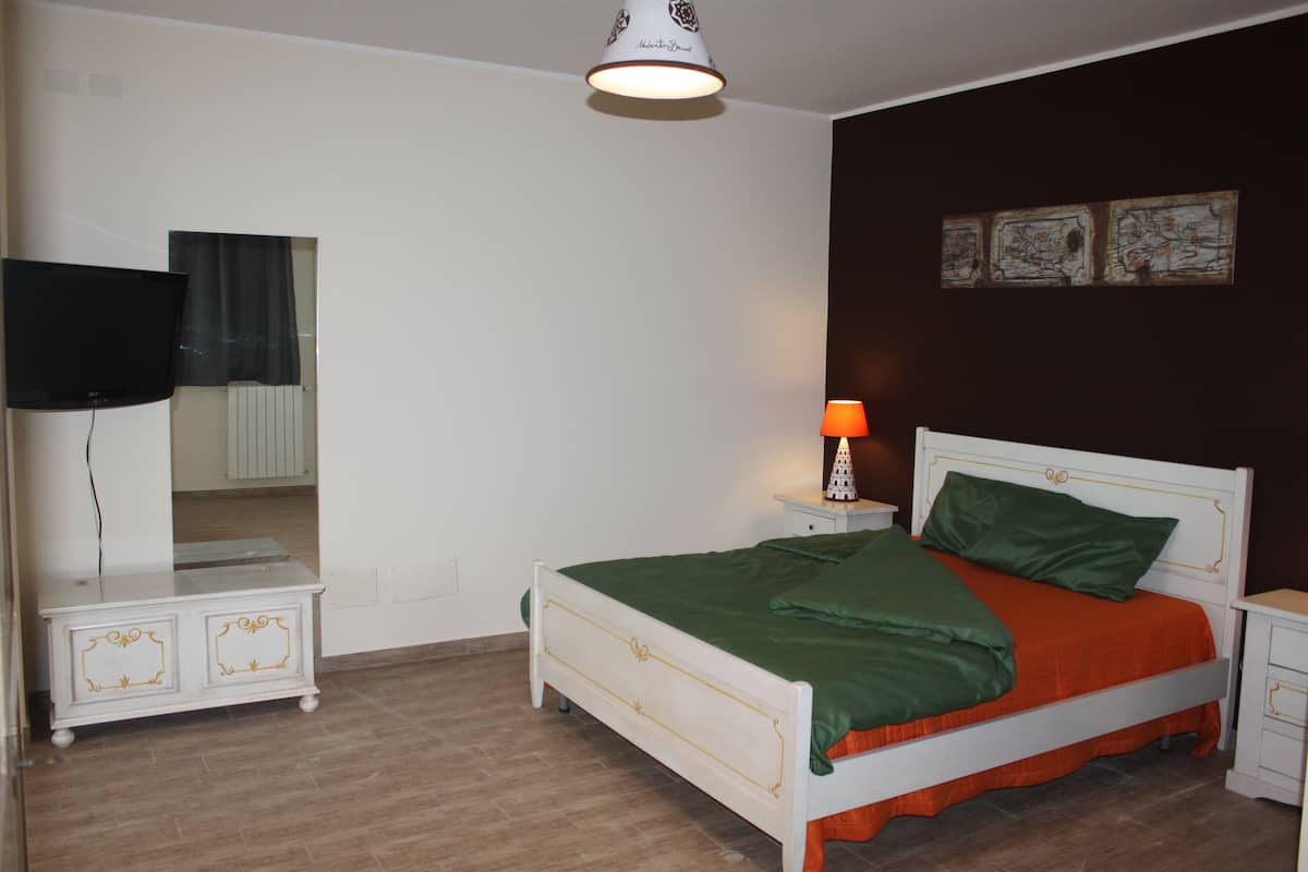 A bedroom with a bed, a nightstand, a lamp, a TV, and a dresser.