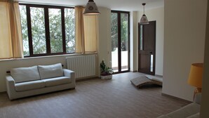 A living room with a sofa, a small table with a plant, a lamp, and a view through large windows. - Locanda Del Drago (Monreale)