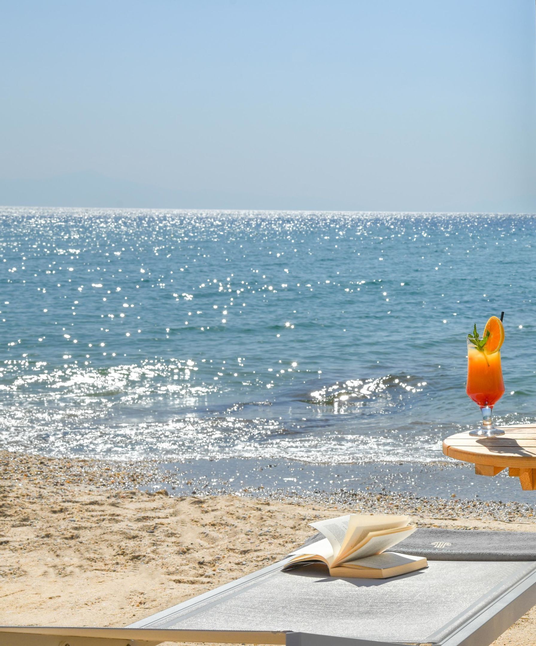 A beach view with a drink on a table and an open book.