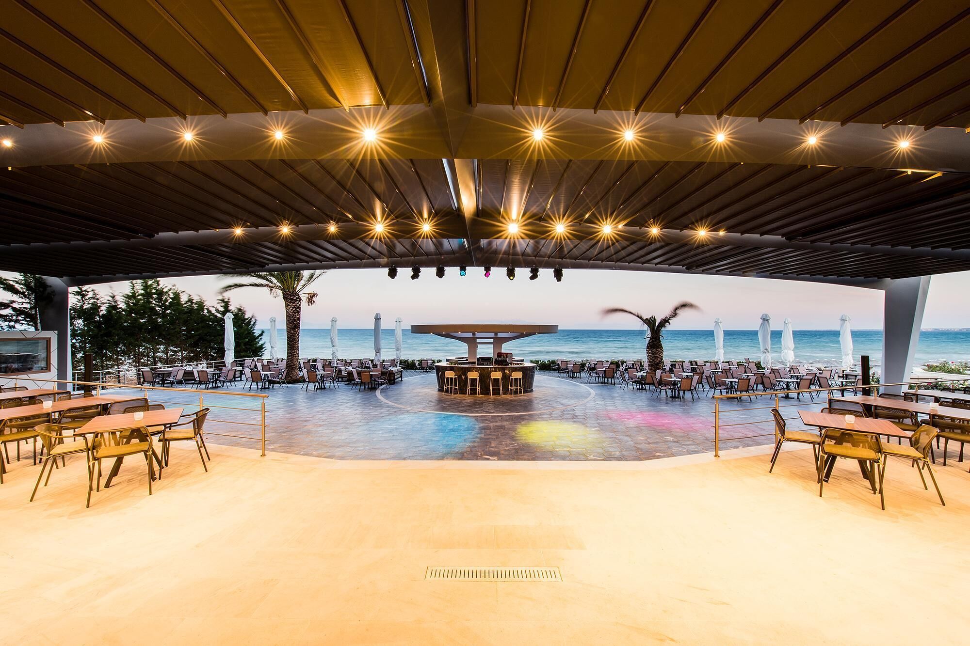Un espace extérieur abrité, aménagé pour les repas, avec un bar, des tables et des chaises, et offrant une vue sur la mer.
