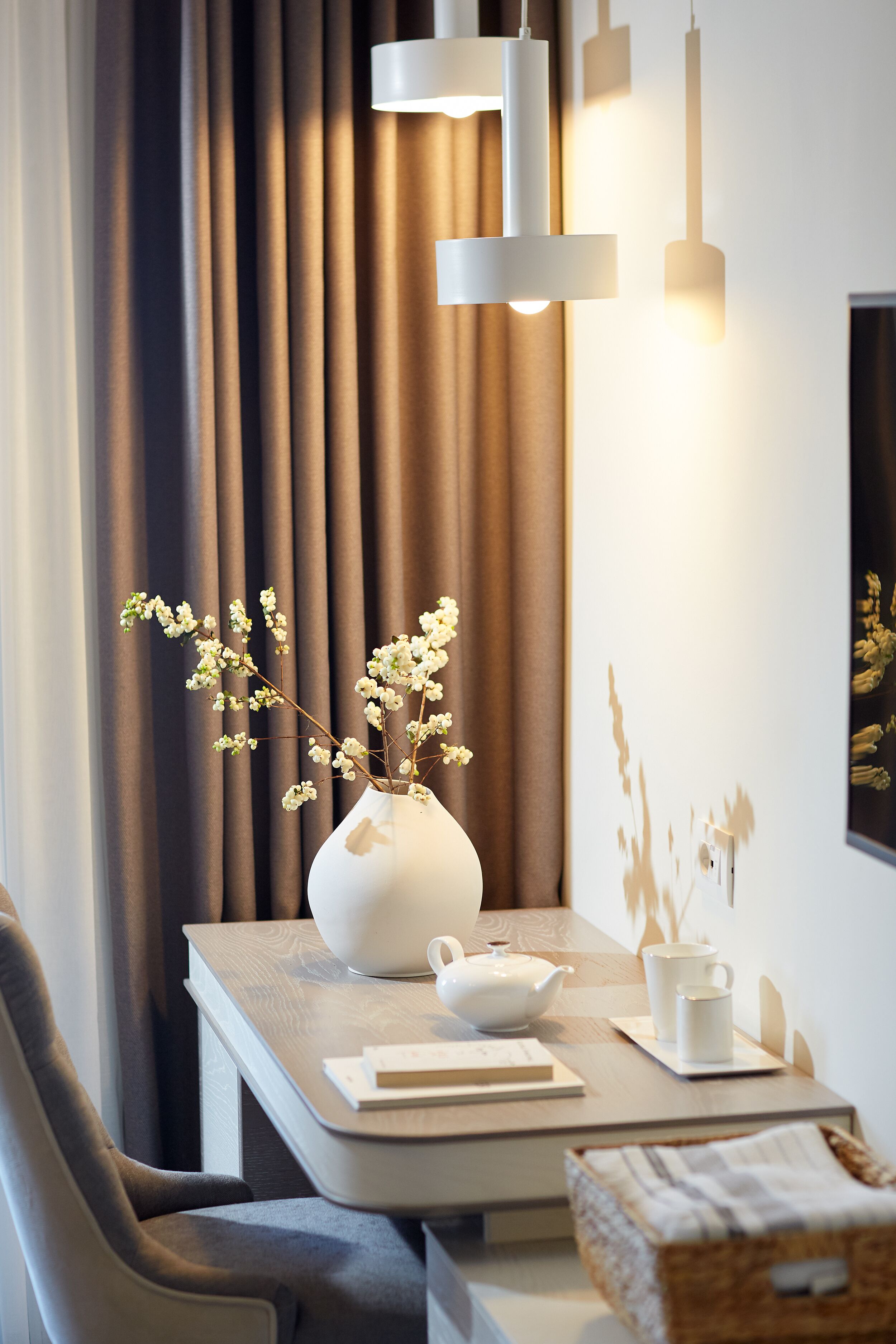 Een moderne eetruimte met een tafel gedekt voor twee personen, met een vaas met bloemen, een theepot en een kopje.