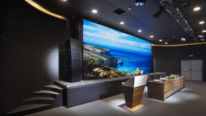 A modern conference room with a large screen displaying a scenic landscape, a reception desk, and a staircase leading to upper levels. - Potidea Palace Hotel - All inclusive (Nea Propontida)