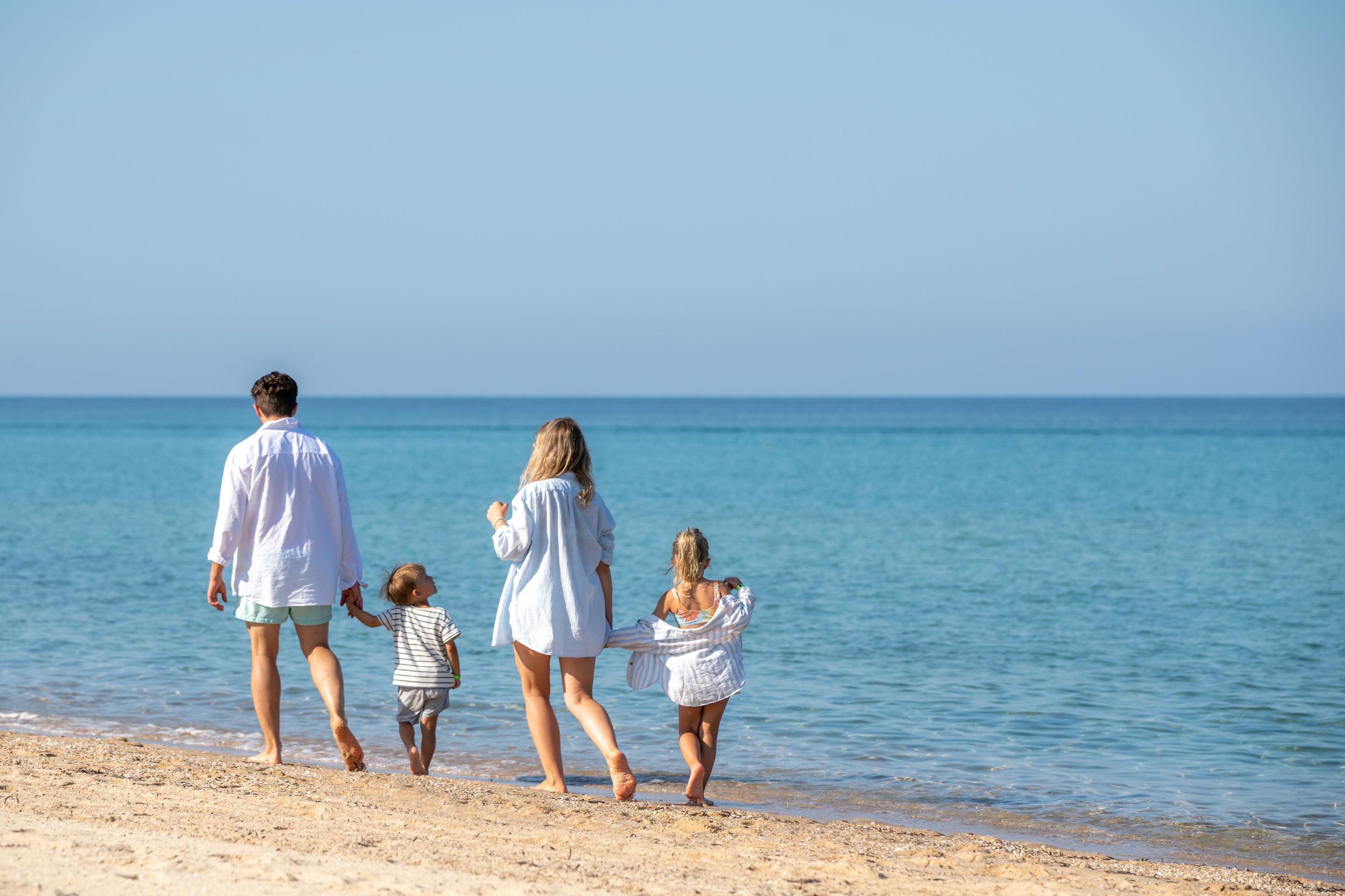 Une famille se promène sur une plage, sous un ciel dégagé.