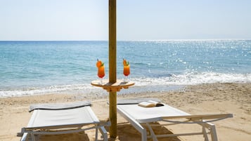 A beachside setting with two lounge chairs, a table with a book, and two drinks on a wooden stand.