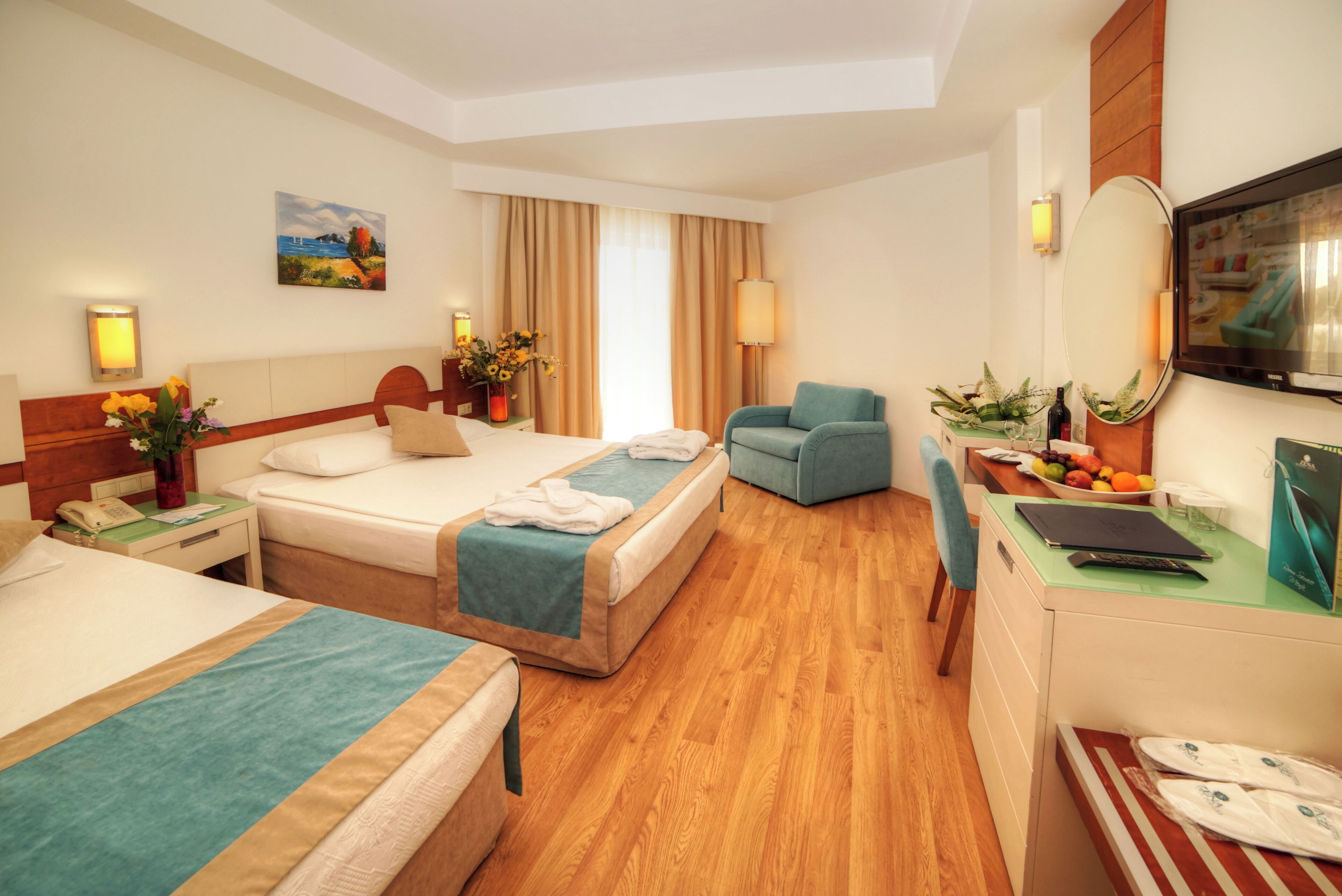 Habitació d'hotel amb dos llits, una taula de treball amb un ordinador portàtil, una cadira, un televisor i una finestra amb cortines.