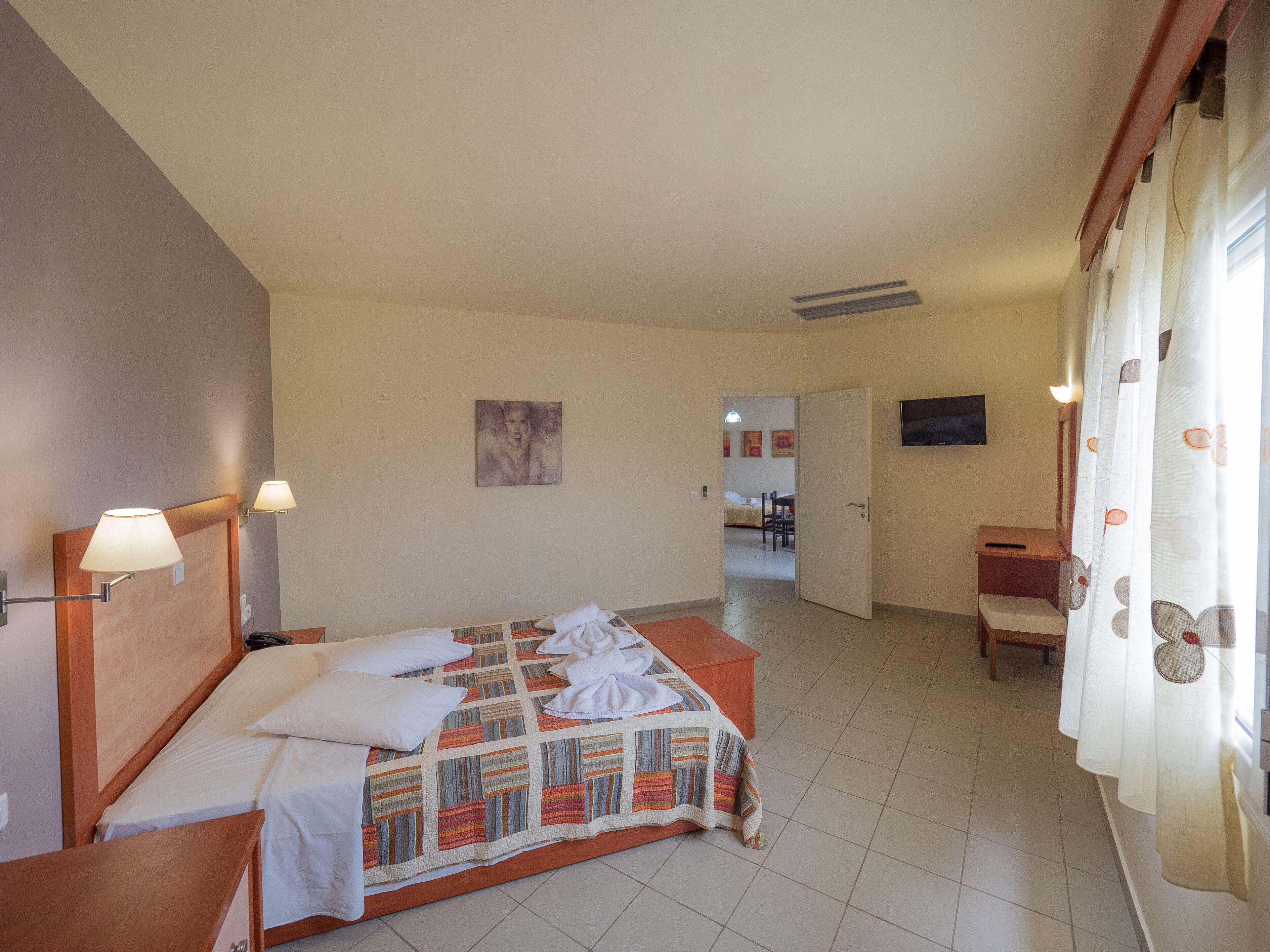 Une chambre d’hôtel avec un lit, un bureau, une chaise, une télévision et une salle de bain visible au fond.