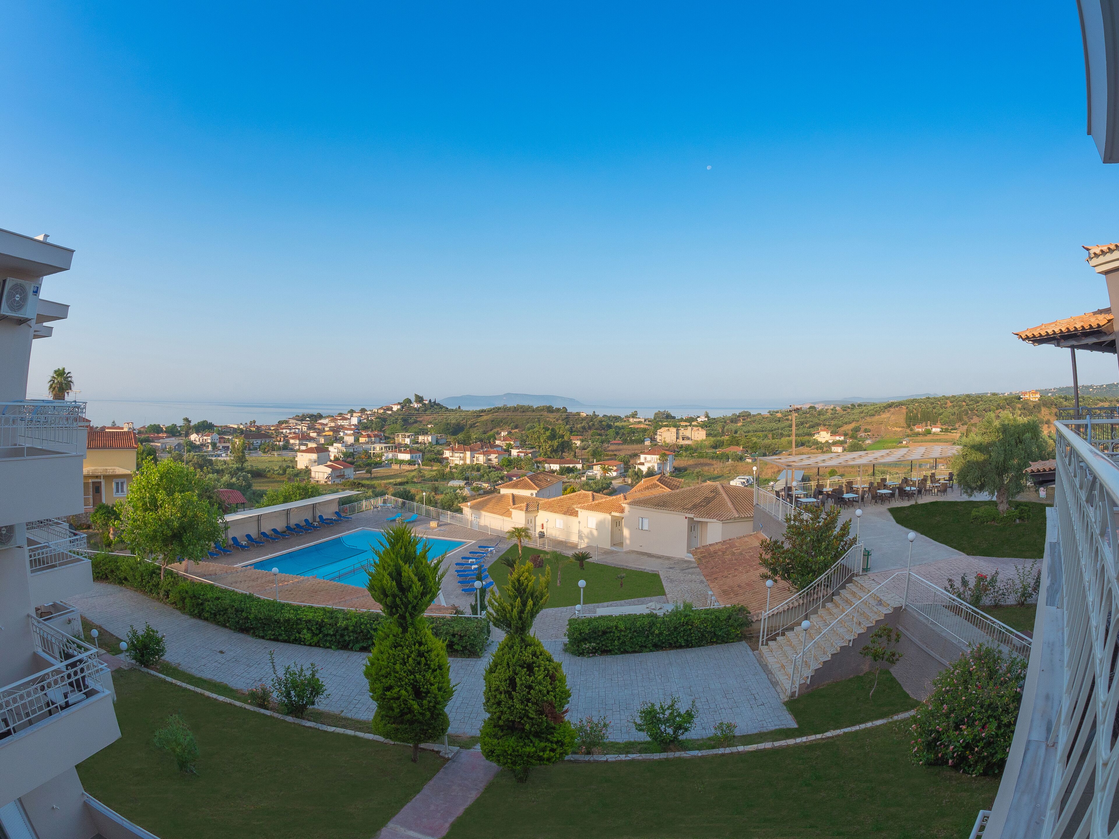 A view of a pool area with a clear sky, surrounded by greenery and buildings.