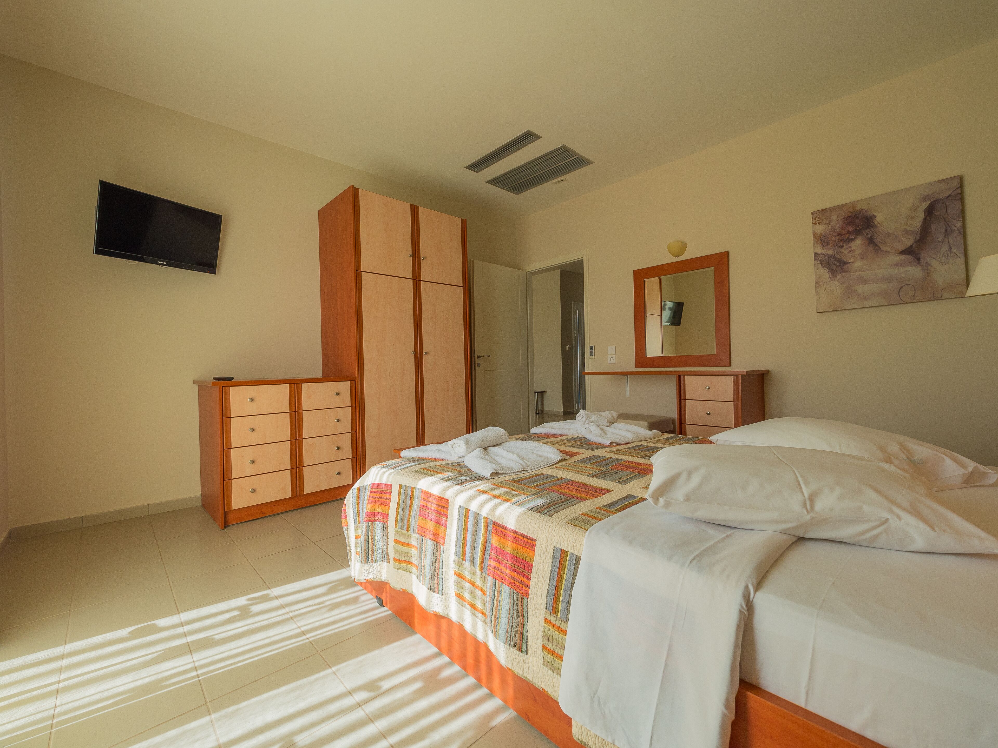 A hotel room with a bed, a wardrobe, a television, and a painting on the wall.