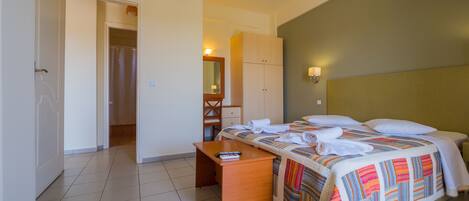 Habitación de hotel con cama, escritorio, espejo y baño visible a través de una puerta abierta.
