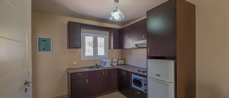A kitchen with dark wooden cabinets, a built-in oven, a white refrigerator, and a window above the sink.