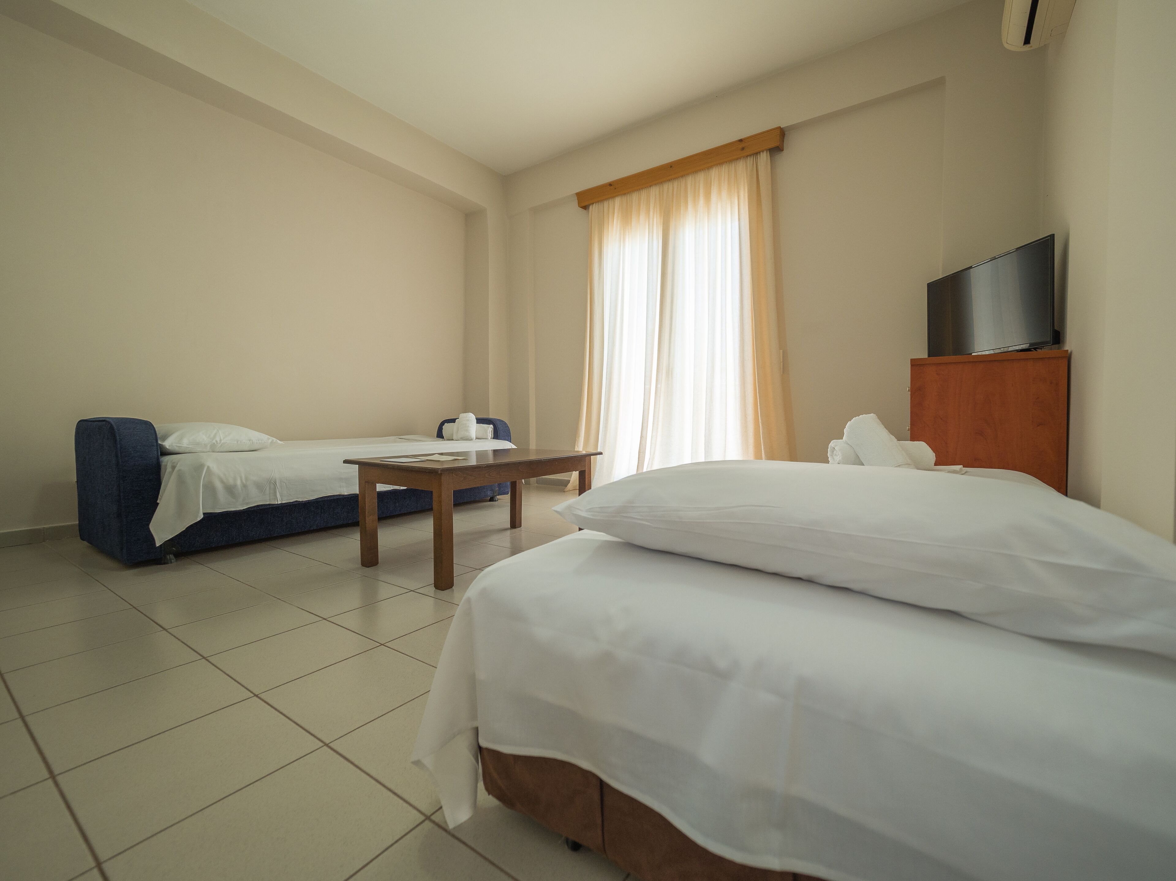 A hotel room with a bed, a sofa, a table, and a TV.