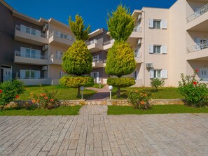 Un patio con dos árboles bien cuidados, un camino pavimentado y un edificio con balcones y ventanas.