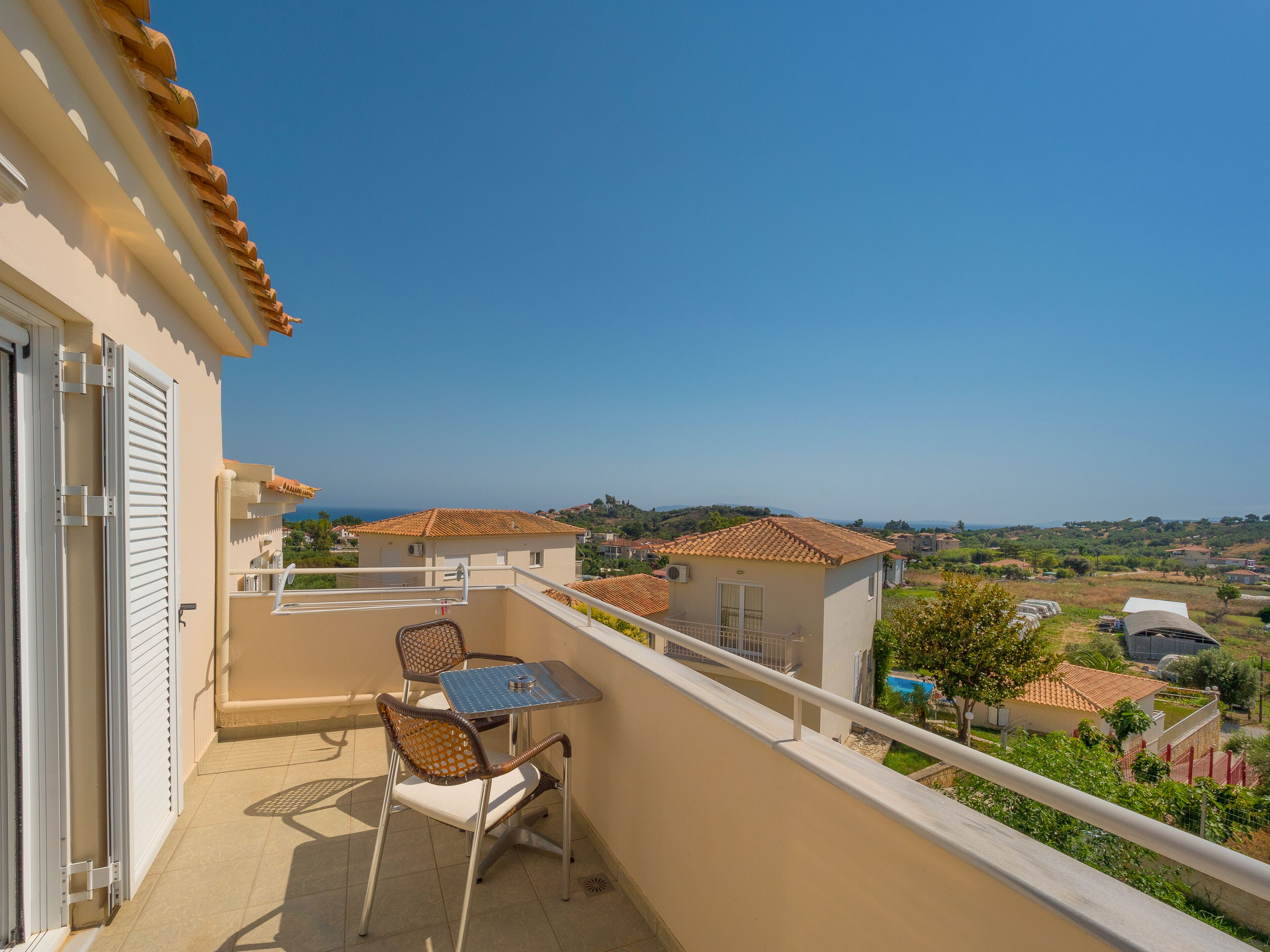 A balcony with a table and chairs, overlooking a residential area with houses and a clear sky.