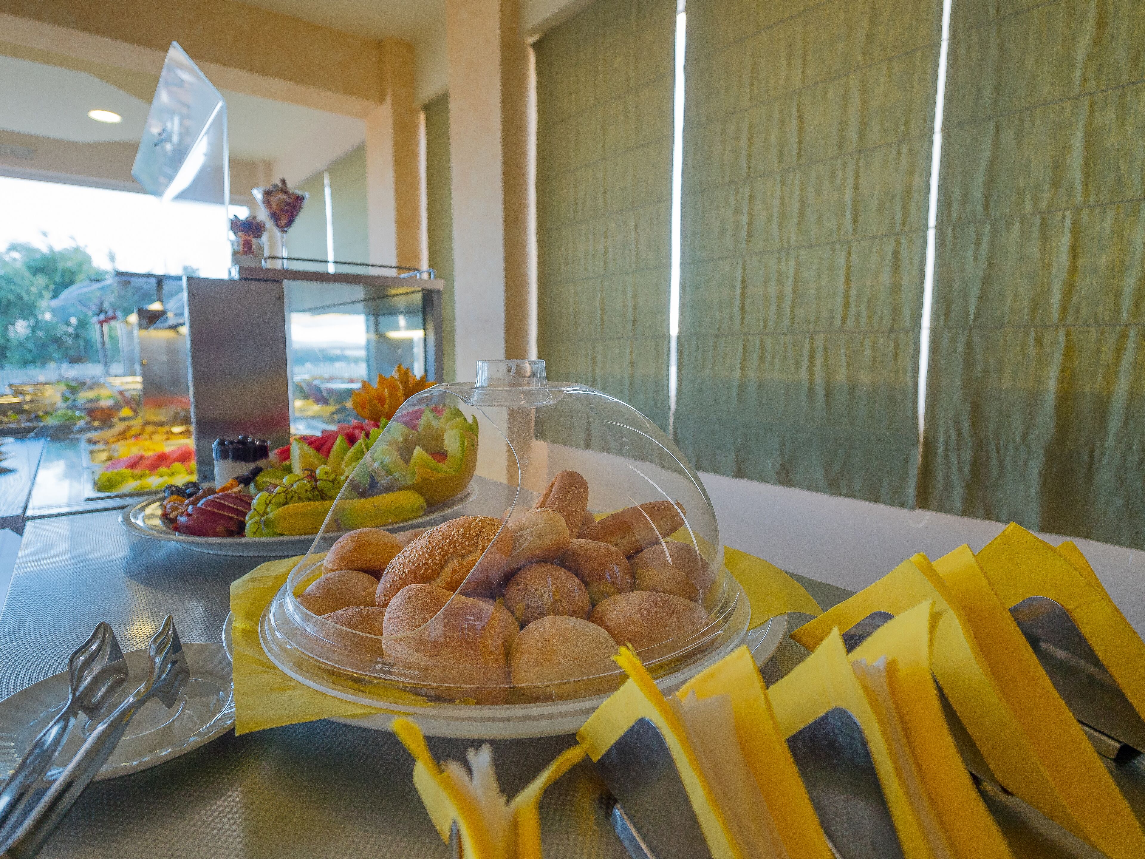 Une table de buffet proposant une variété de plats, notamment du pain et des fruits, le tout recouvert d’un couvercle en verre.